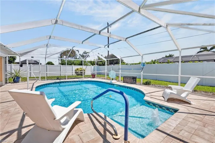 Screened enclosure with an in-ground swimming pool, decorative tile border, water feature, and paved pool deck