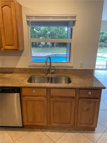 Kitchen with stainless steel dishwasher, light tile patterned flooring, brown cabinets, and a sink
