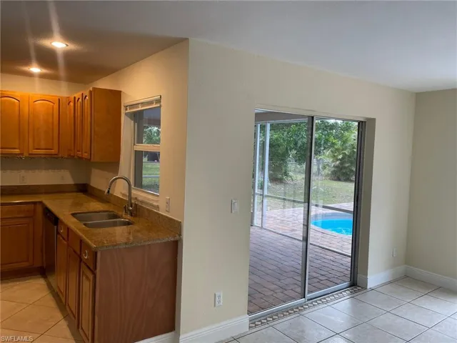 Kitchen featuring brown cabinets, a sink, stainless steel dishwasher, light tile patterned floors, and baseboards