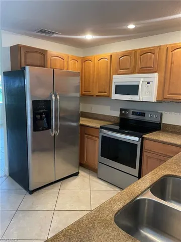 Kitchen featuring a sink, appliances with stainless steel finishes, brown cabinetry, and light tile patterned floors