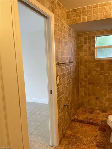 Full bath featuring tile patterned floors, tiled shower, and toilet