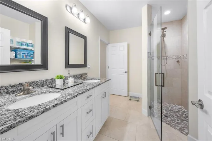 Bathroom featuring double vanity, a stall shower, and light tile patterned flooring