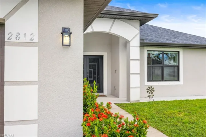 Property entrance featuring roof with shingles, stucco siding, and a lawn