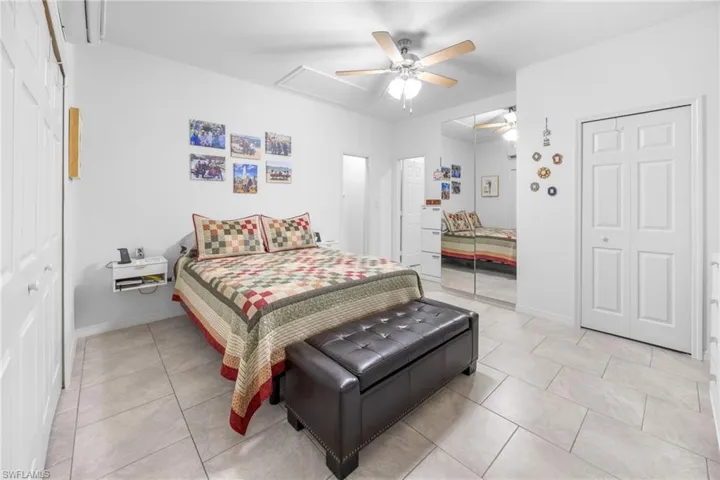 Bedroom with ceiling fan, attic access, light tile patterned flooring, and a wall mounted air conditioner