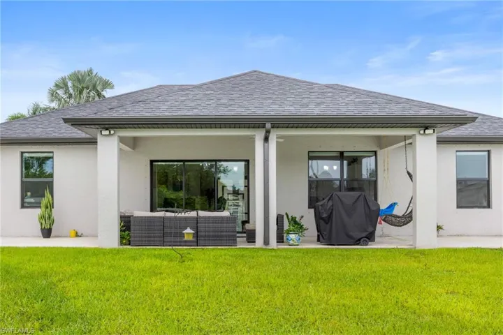 Rear view of house featuring a shingled roof, a patio, stucco siding, and a lawn