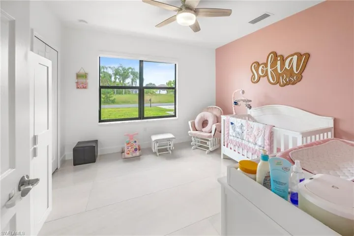 Bedroom featuring a crib, light tile patterned floors, and ceiling fan