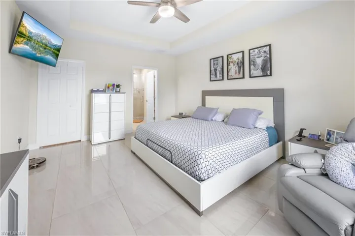 Tiled bedroom featuring a tray ceiling, ceiling fan, and ensuite bathroom