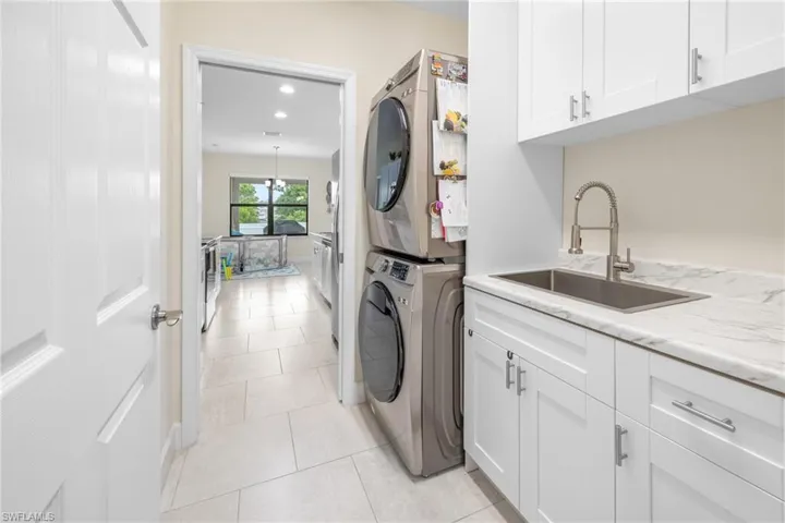 Laundry area with cabinet space, light tile patterned flooring, estacked washer and dryer, and recessed lighting