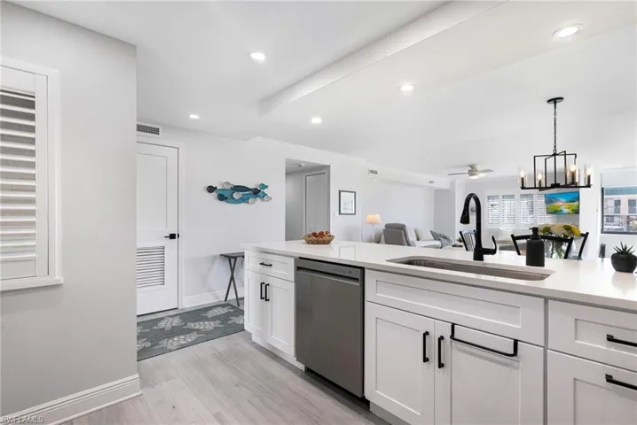 Kitchen featuring sink, light hardwood / wood-style floors, decorative light fixtures, stainless steel dishwasher, and white cabinets