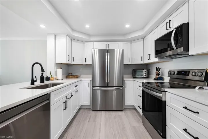 Kitchen with appliances with stainless steel finishes, sink, white cabinetry, ornamental molding, and light hardwood / wood-style flooring