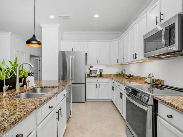 Kitchen featuring white cabinets, appliances with stainless steel finishes, hanging light fixtures, and sink