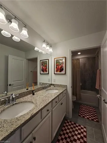 Bathroom featuring shower / bath combination with curtain, double vanity, a textured ceiling, and dark tile patterned floors