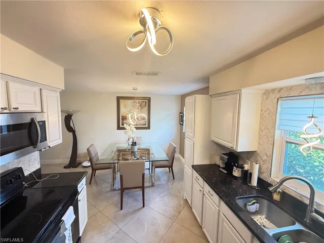 Kitchen with black electric range, hanging light fixtures, decorative backsplash, and stainless steel microwave