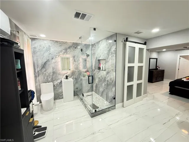 Bathroom with light marble finish floors, recessed lighting, a marble finish shower, and tile walls