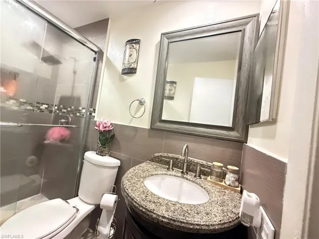 Bathroom featuring vanity, a shower stall, wainscoting, and tile walls