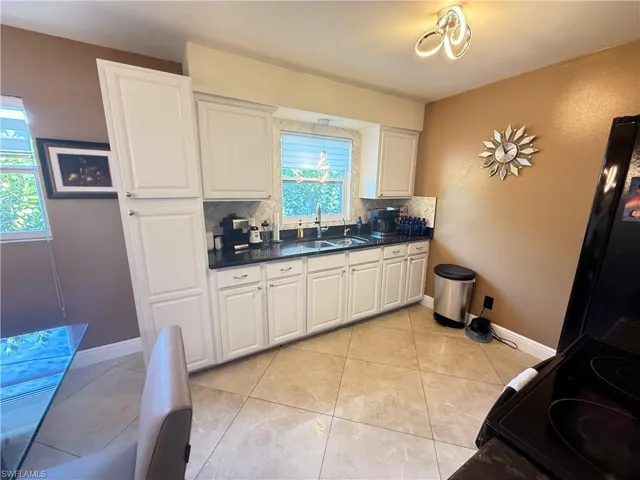 Kitchen with white cabinetry, electric range, light tile patterned flooring, and backsplash