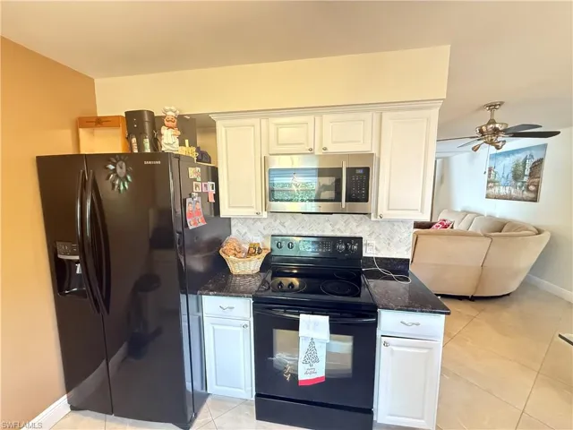Kitchen with black appliances, dark stone counters, light tile patterned floors, and tasteful backsplash