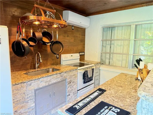 Kitchen featuring light stone countertops, white appliances, a wall mounted air conditioner, wood ceiling, and a textured wall