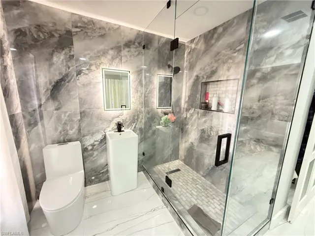 Full bath featuring marble tiled floors, tile walls, and a marble finish shower