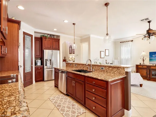 Kitchen featuring stainless steel appliances, light stone countertops, hanging light fixtures, crown molding, and light tile patterned floors