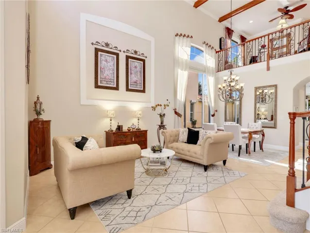 Tiled living area with a ceiling fan, a chandelier, arched walkways, a high ceiling, and ornamental molding