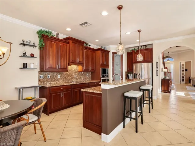 Kitchen featuring a breakfast bar, arched walkways, light stone countertops, light tile patterned floors, and crown molding
