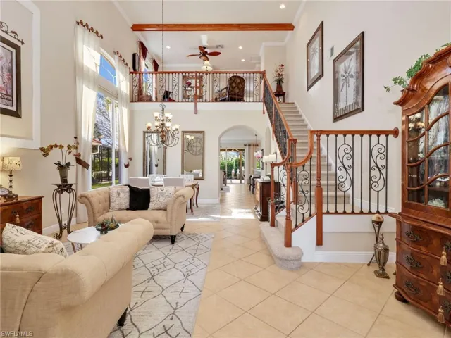 Tiled living room featuring arched walkways, hanging lights, crown molding, a high ceiling, and a ceiling fan