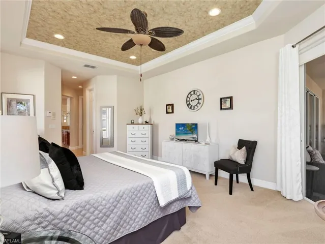 Bedroom featuring a raised ceiling, ensuite bathroom, light carpet, a ceiling fan, and ornamental molding