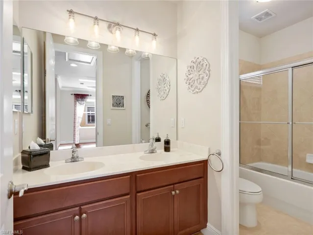 Full bath featuring shower / bath combination with glass door, double vanity, and light tile patterned floors