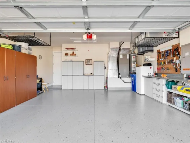Garage featuring freestanding refrigerator, electric panel, water heater, and a garage door opener