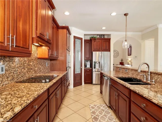 Kitchen with light stone counters, hanging light fixtures, stainless steel appliances, crown molding, and decorative backsplash
