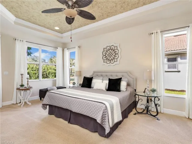 Bedroom with light colored carpet, a tray ceiling, ornamental molding, and a ceiling fan
