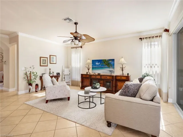 Living area with crown molding, plenty of natural light, a ceiling fan, and light tile patterned floors