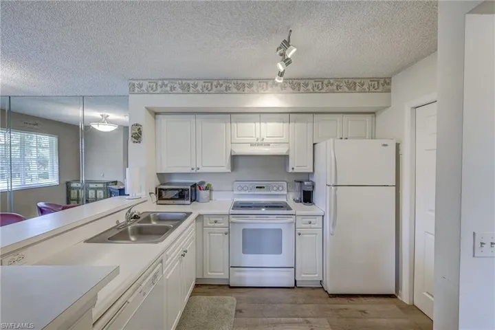 Kitchen featuring white cabinetry, solid-surface countertops, dual-basin stainless steel sink, electric range, and wood-finish flooring