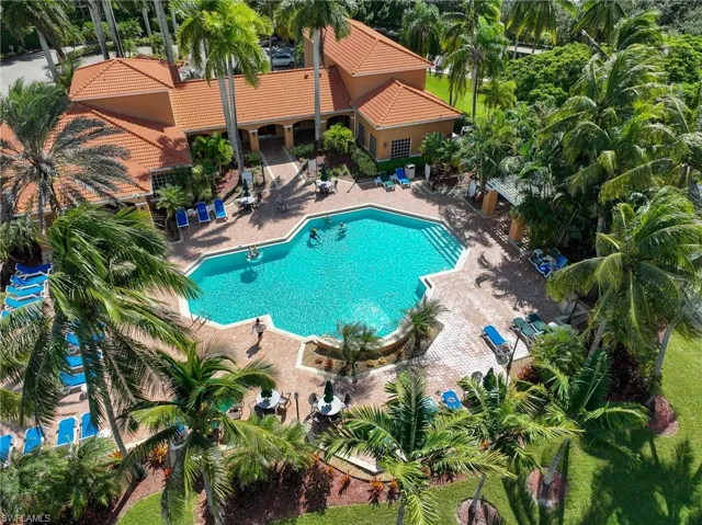 Stucco exterior with a tiled roof, surrounding an expansive swimming pool, brick-paved patio, and mature landscaping