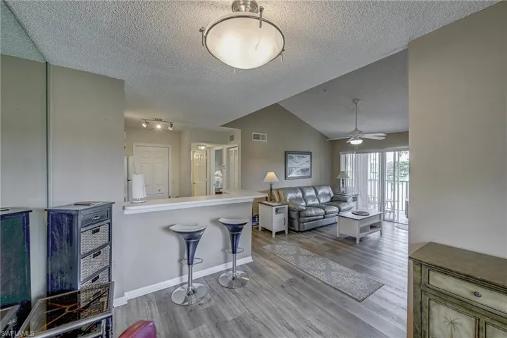 Living area featuring vaulted ceilings, wood-finish flooring, a breakfast bar, and sliding glass doors