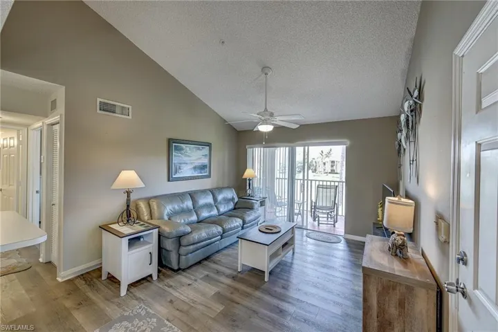 Living area featuring vaulted ceilings, wood-finish flooring, a ceiling fan with integrated lighting, and sliding glass doors with vertical blinds