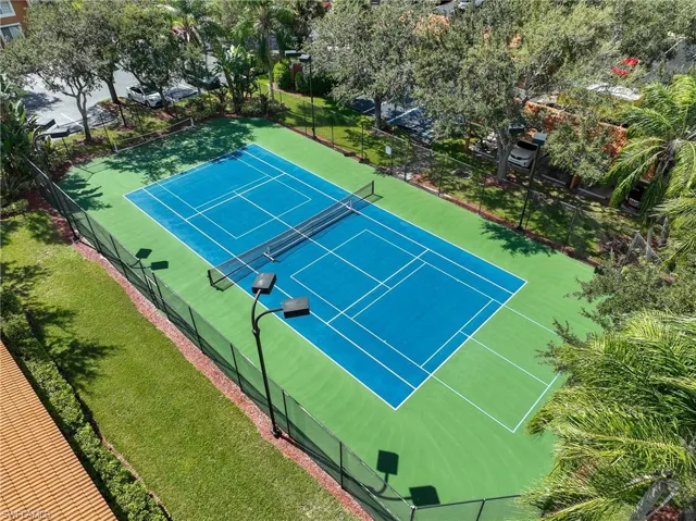 Tennis court featuring a high-contrast blue and green acrylic surface, chain-link perimeter fencing, and overhead court lighting
