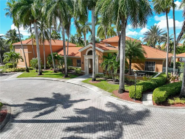 Stucco exterior featuring a tile roof, arched entryway with decorative columns, paver driveway, and mature palm landscaping