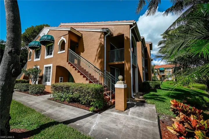 Stucco exterior featuring arched architectural detailing, metal stair railing, decorative window awnings, and landscaped grounds