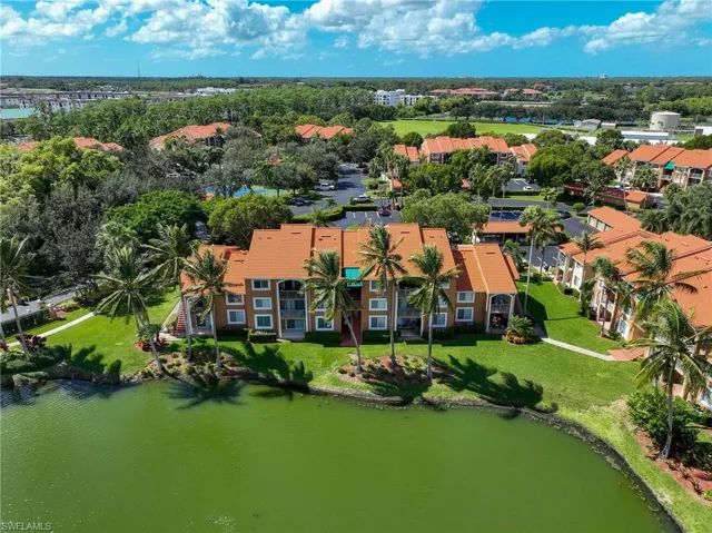 Aerial perspective of multi-story buildings featuring clay tile roofs, terracotta-tone facades, landscaped green spaces, and direct water frontage with mature palm trees