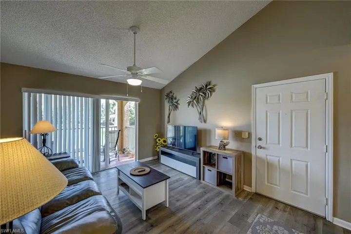 Vaulted ceilings featuring a central white ceiling fan and light fixture, complemented by wood-finish flooring and sliding glass door access to a covered balcony