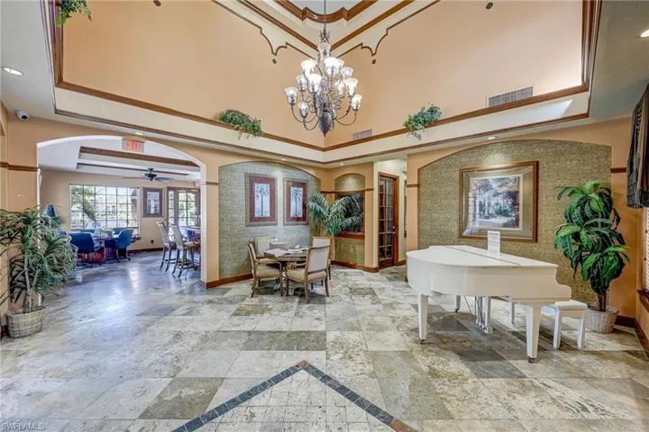Grand foyer featuring a vaulted ceiling with crown molding, natural stone tile flooring, a multi-tiered crystal chandelier, and arched wall alcoves with textured decorative wallpaper