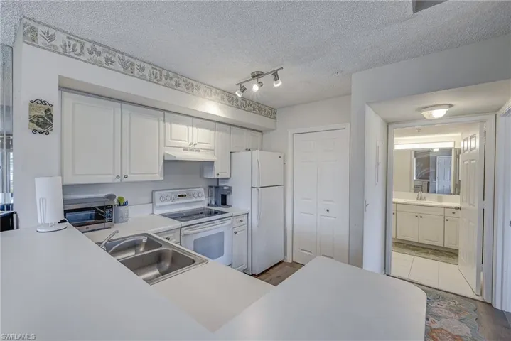 Kitchen featuring white cabinetry, solid-surface countertops, dual-basin stainless steel sink, and track lighting