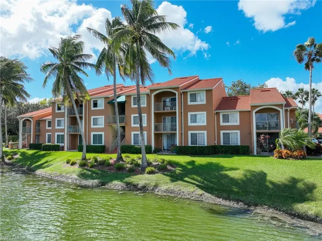 Multi-story exterior featuring a tile roof, private balconies with metal railings, and waterfront grounds with mature palm trees