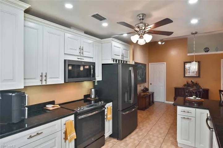 Kitchen with raised panel cabinetry with crown molding, recessed lighting, stainless appliances, and black granite countertops.