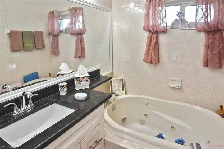 Bathroom featuring a relaxing soaker tub with jets, granite vanity, and tile walls