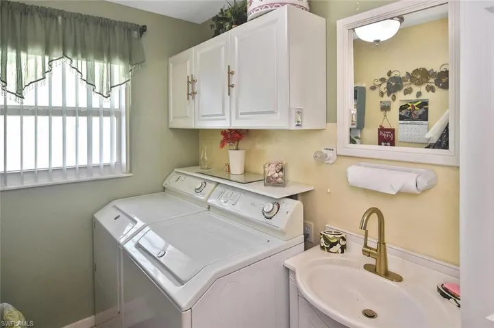Laundry area featuring washer and clothes dryer and a sink.  Additional storage is on the opposite wall.