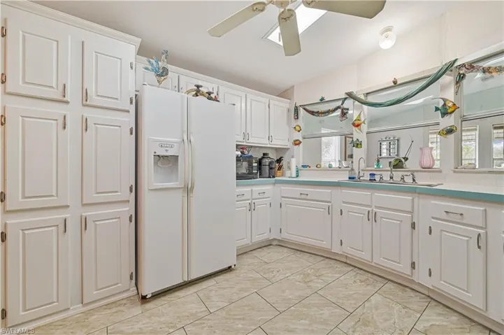 Kitchen featuring light countertops, a sink, white refrigerator with ice dispenser, white cabinetry, and ceiling fan
