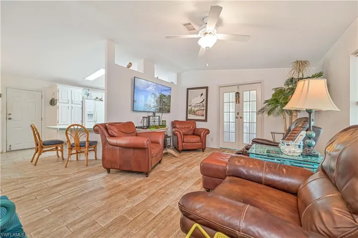 Living room featuring visible vents, ceiling fan, light wood-style flooring, and vaulted ceiling